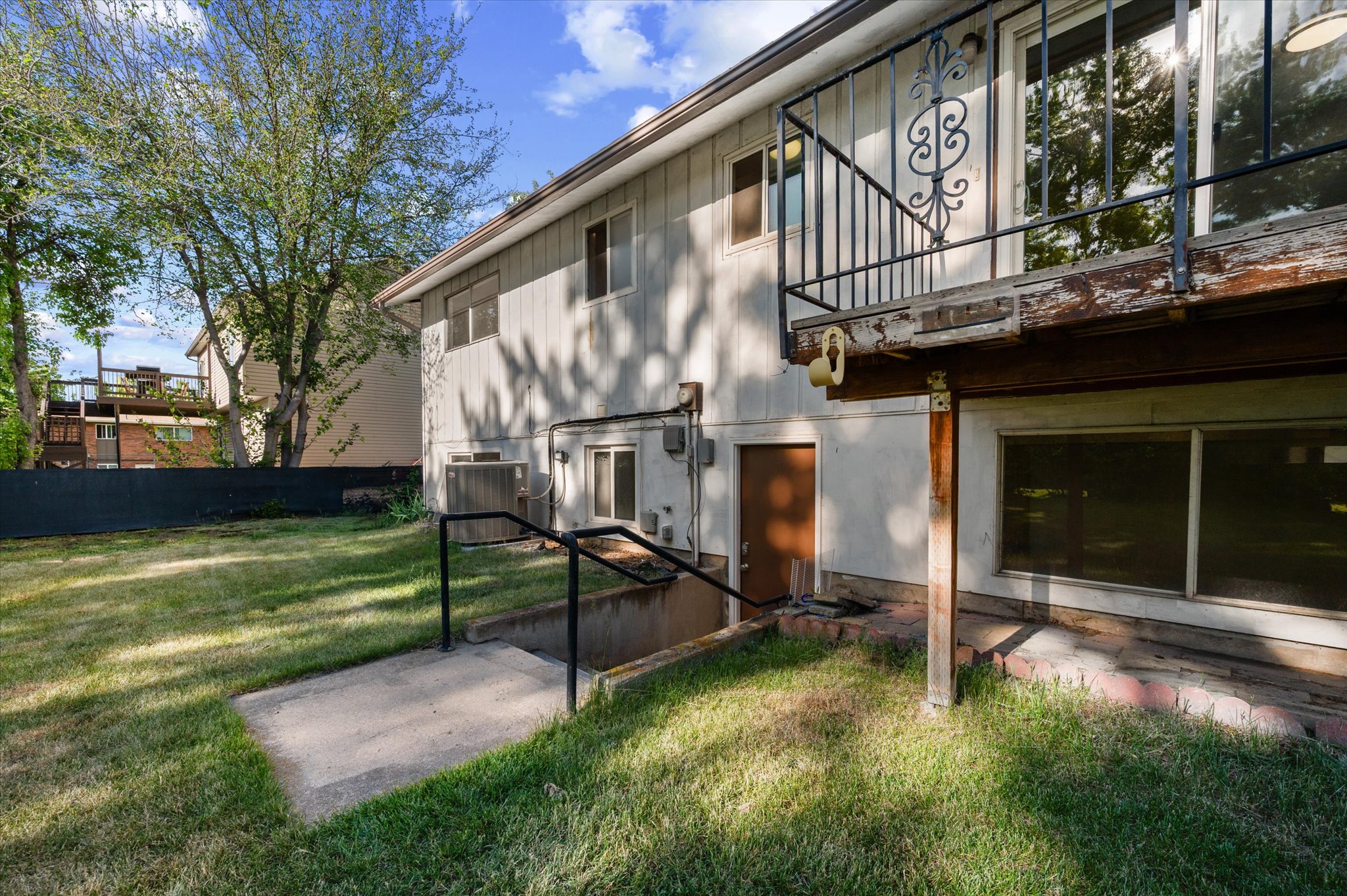 Rear exterior featuring a ground-level patio, a set of concrete stairs with metal railings, walkout basement entrance and a second-story deck with decorative metalwork