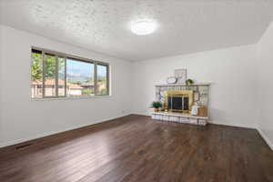Spacious room featuring wood-finish flooring, a large multi-pane window, and a stone fireplace with a brass firebox
