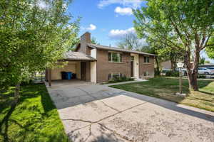 Brick exterior residence featuring a covered carport, mature trees, a concrete driveway, and a front lawn