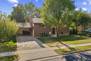 Brick exterior residence featuring a carport, mature trees, and a front lawn