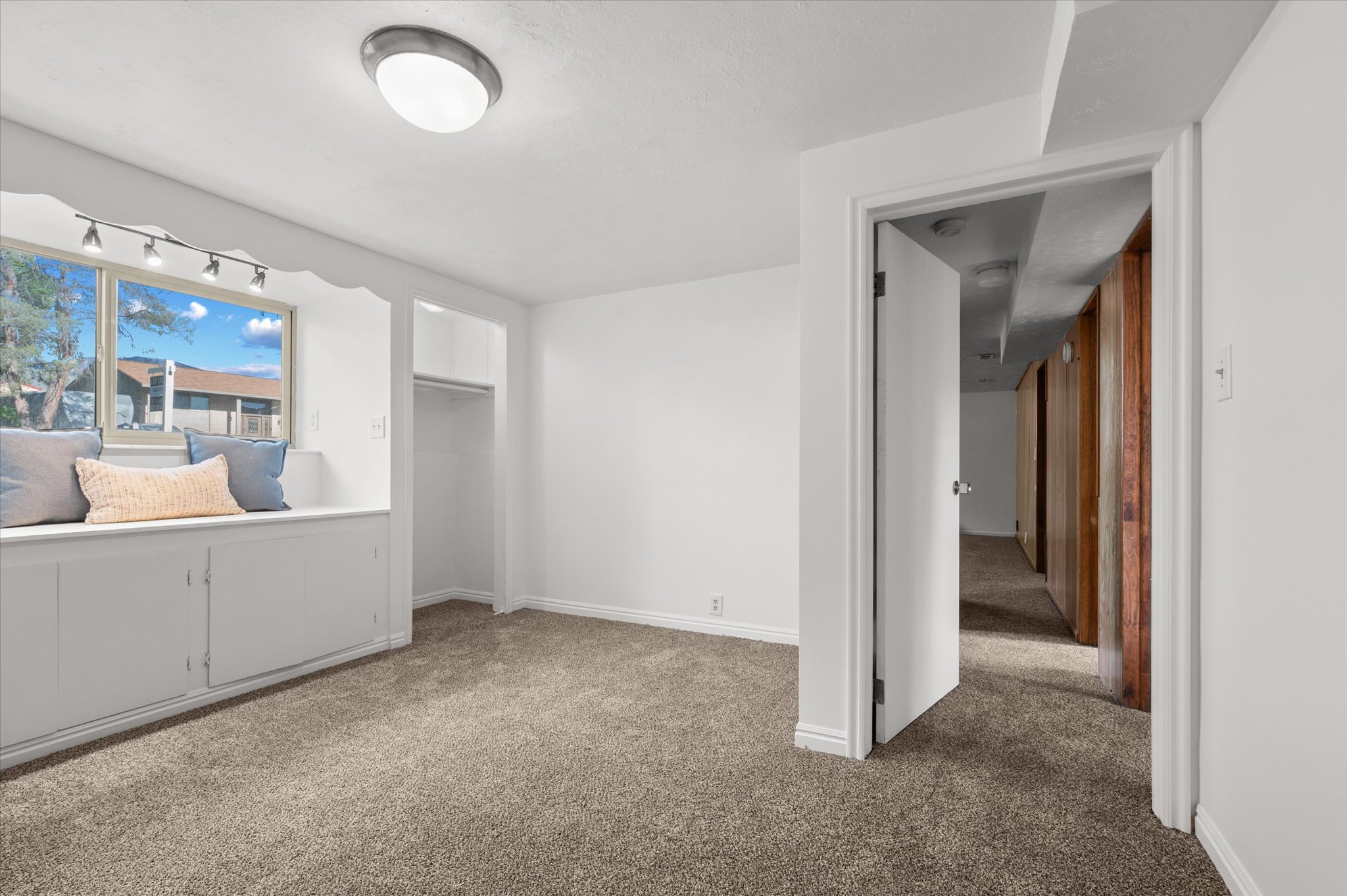Bedroom featuring a window seat with integrated storage, track lighting, and a built-in closet with an open doorway