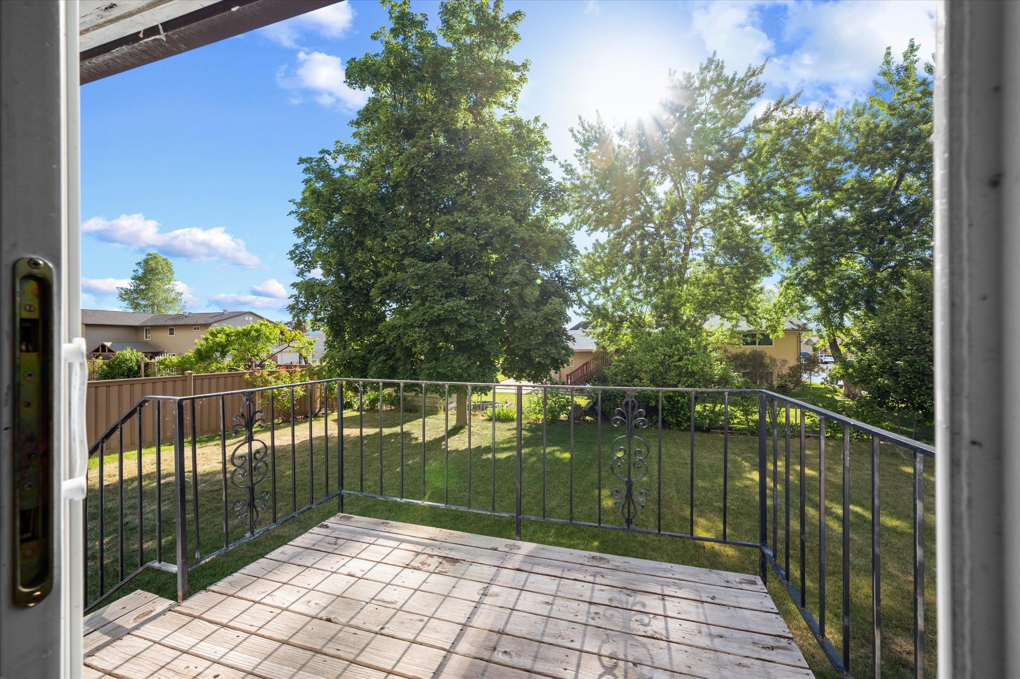 Expansive backyard featuring a manicured lawn, mature trees, and a wooden deck with wrought iron railing