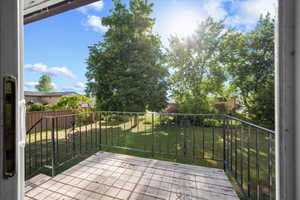 Expansive backyard featuring a manicured lawn, mature trees, and a wooden deck with wrought iron railing