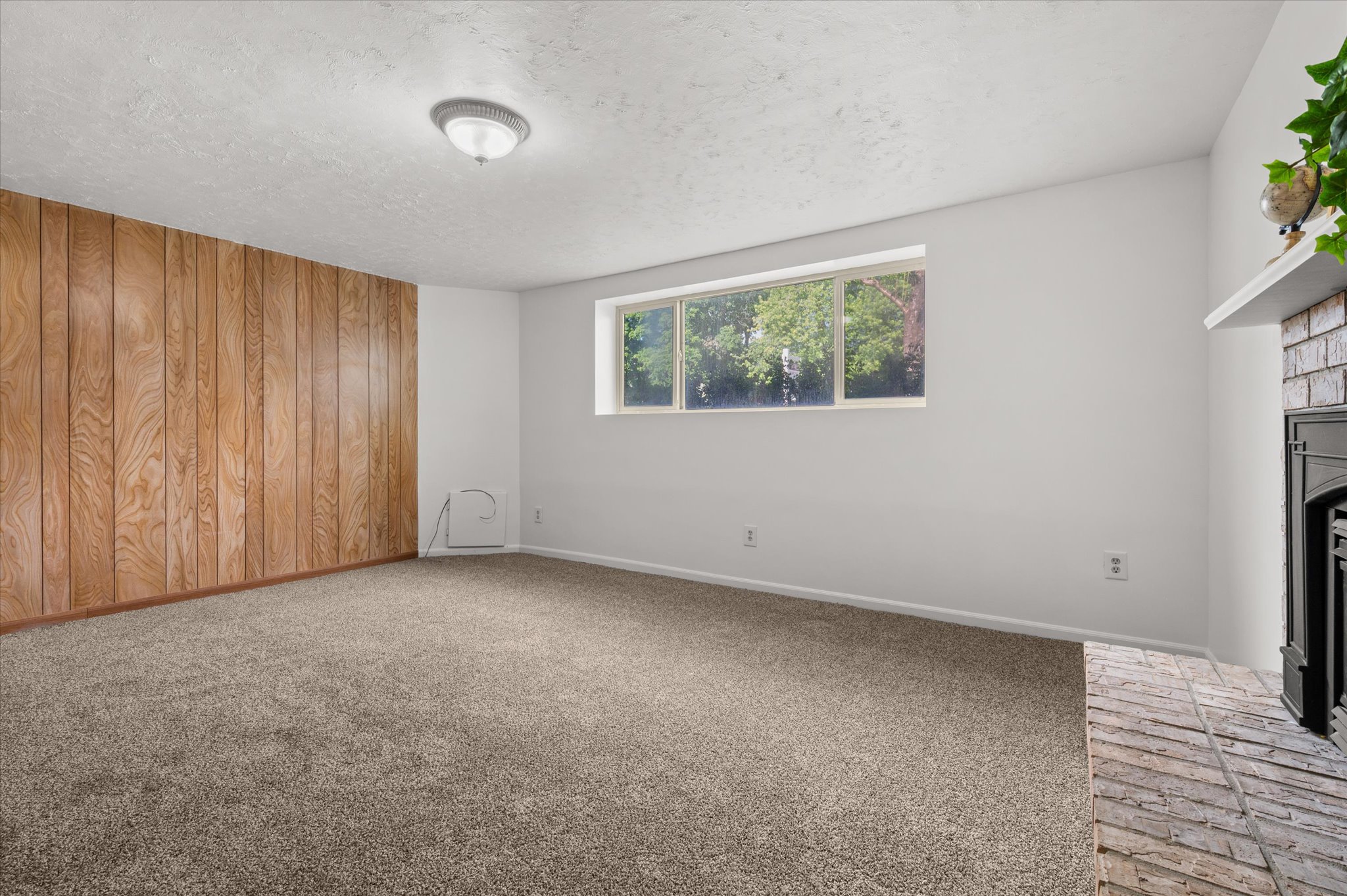 Spacious room featuring wood paneling, light gray carpeting, and a brick fireplace with a black insert