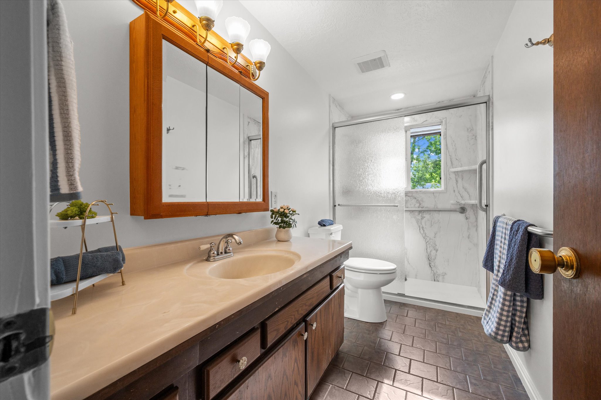 Bathroom featuring a spacious vanity with integrated sink, a wood-framed medicine cabinet, and a shower enclosure with sliding glass doors