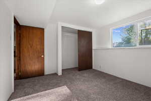 Carpeted room featuring a white ceiling and walls, a window with exterior views, a built-in closet with sliding wood doors, and an additional wood door
