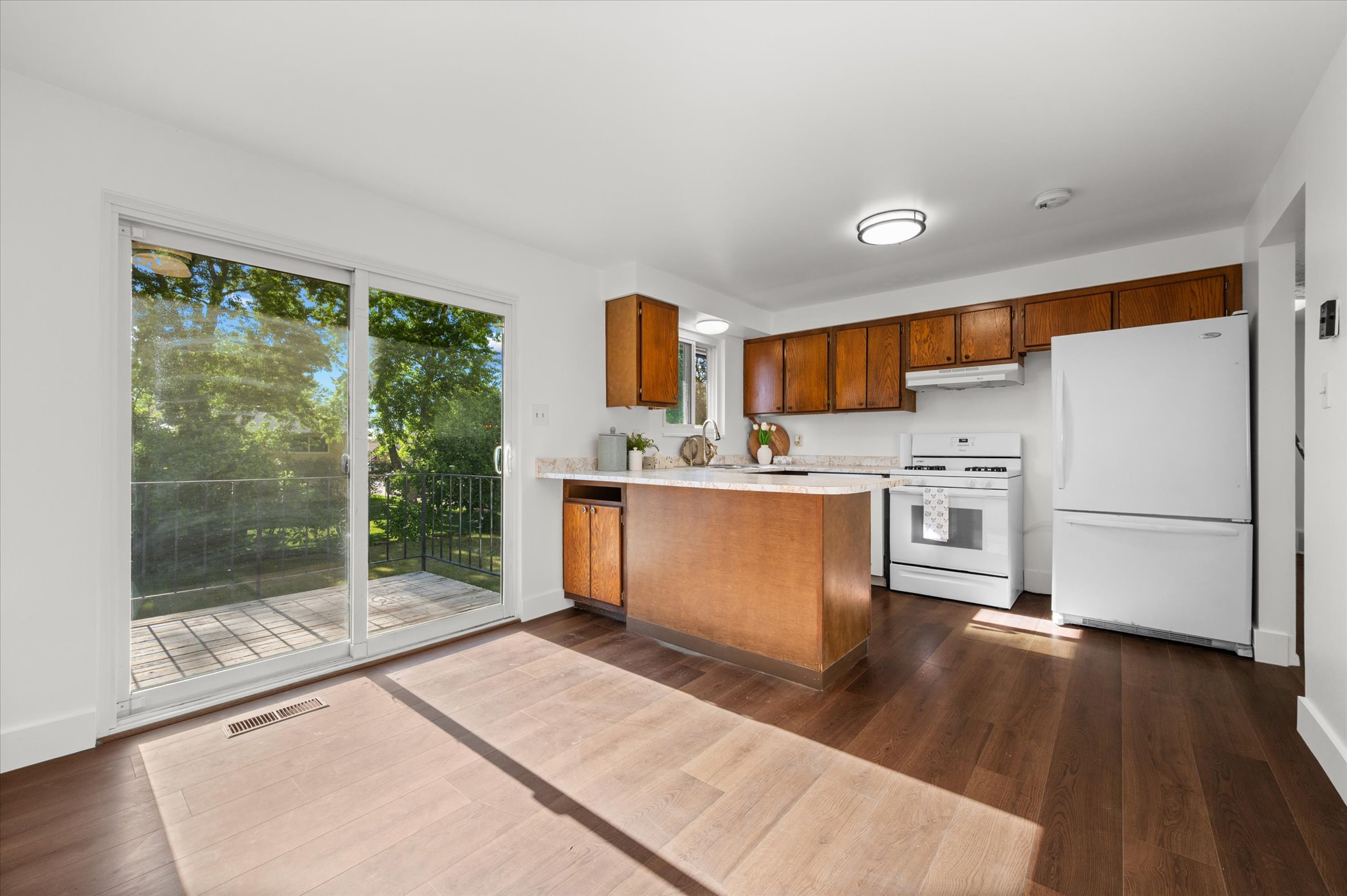 Kitchen with wood-finish flooring, white appliances, and warm wood cabinetry