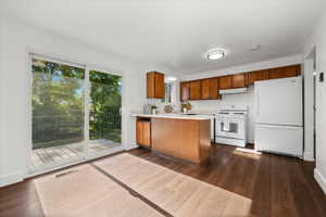 Kitchen with wood-finish flooring, white appliances, and warm wood cabinetry