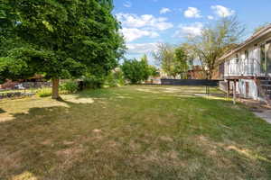 Expansive backyard featuring a mature shade tree, a level lawn, a privacy fence, and a deck with metal railings