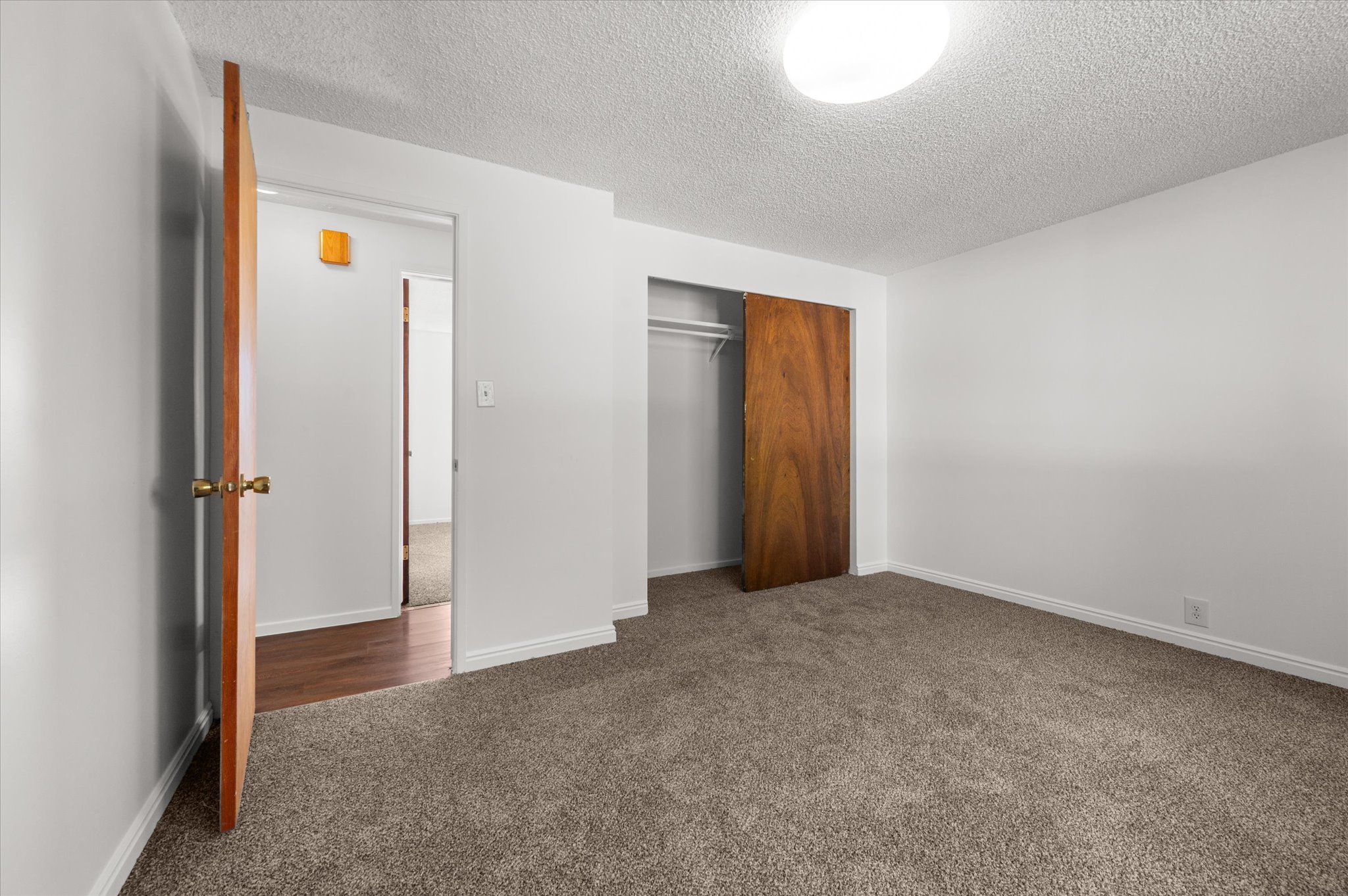 Bedroom featuring plush carpet flooring, white painted walls, a sliding wood-panel closet door, an overhead flush-mount light fixture, and a wood-finish door with brass hardware