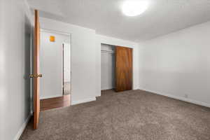 Bedroom featuring plush carpet flooring, white painted walls, a sliding wood-panel closet door, an overhead flush-mount light fixture, and a wood-finish door with brass hardware