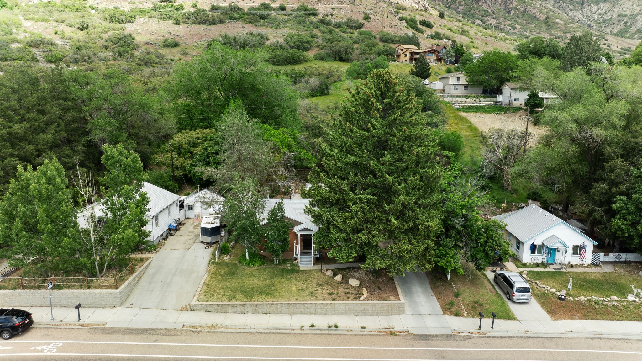 Property featuring two distinct structures, a white siding home, and a brick-front home, set against a verdant hillside