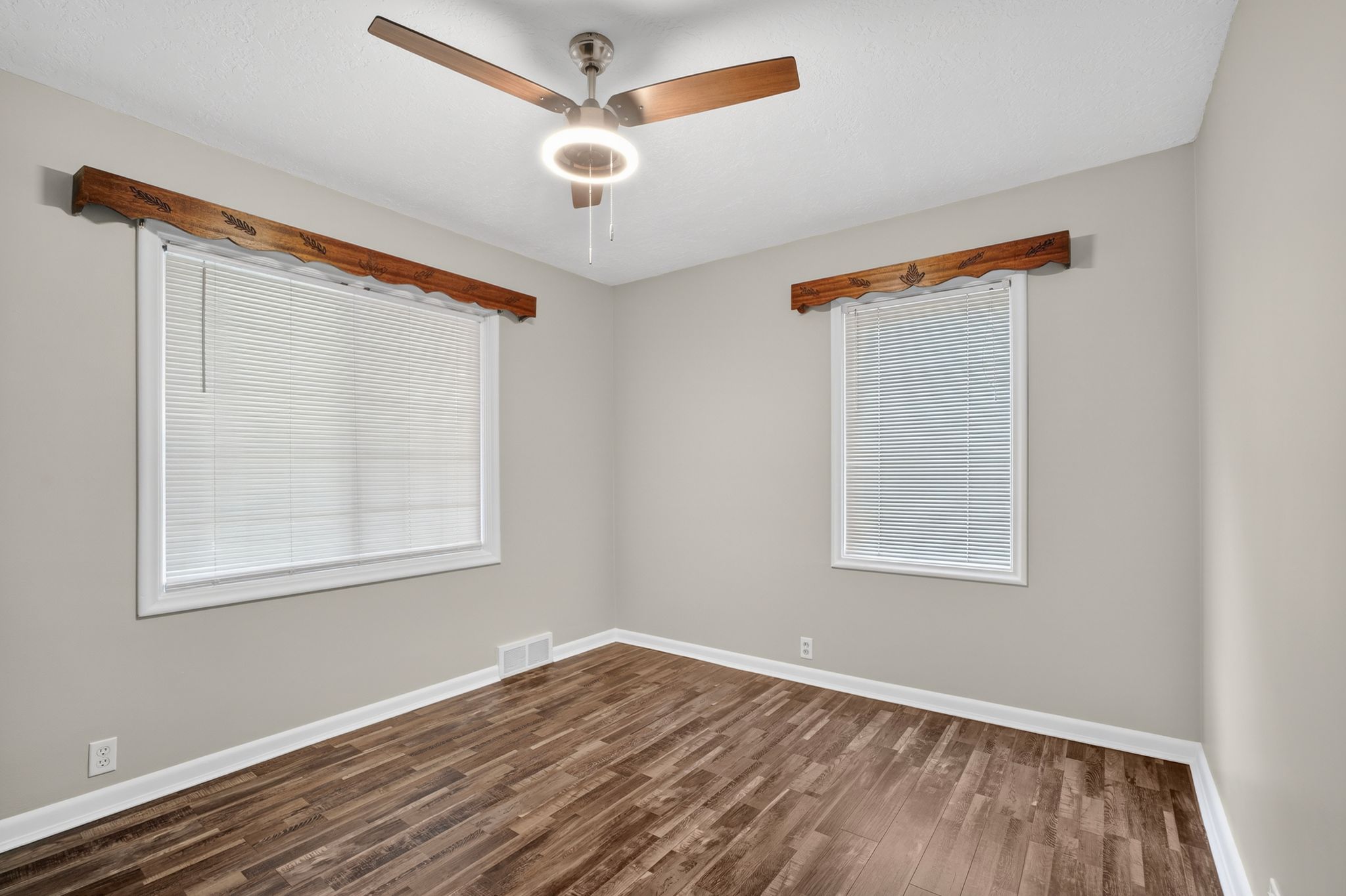 Room featuring wood-finish flooring, two windows with blinds, and white trim