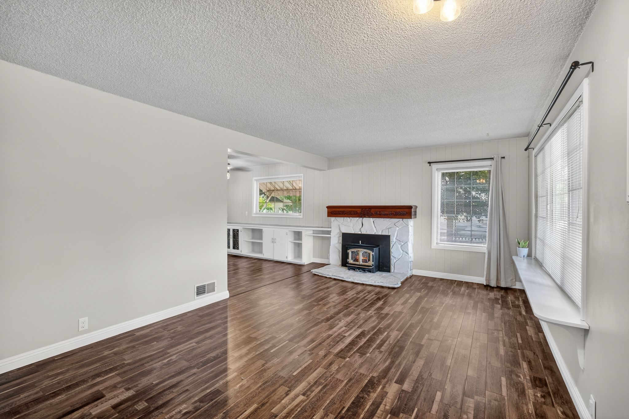 Spacious living area featuring wood-finish flooring, a stone-clad fireplace with a wood mantel, and expansive windows