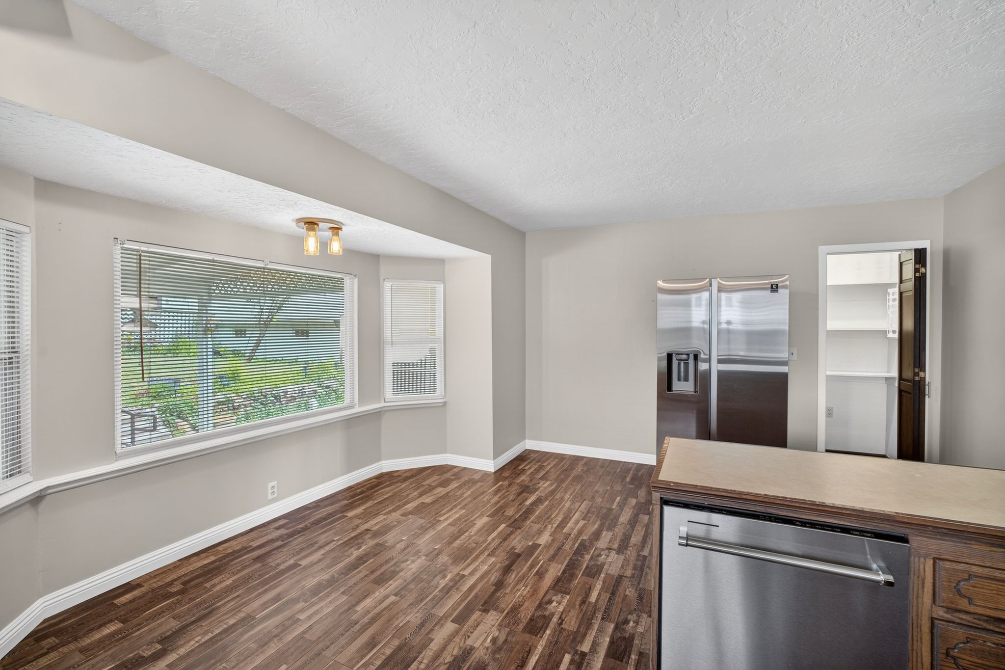 Spacious eating area featuring wood-finish flooring and a wide bay window with blinds
