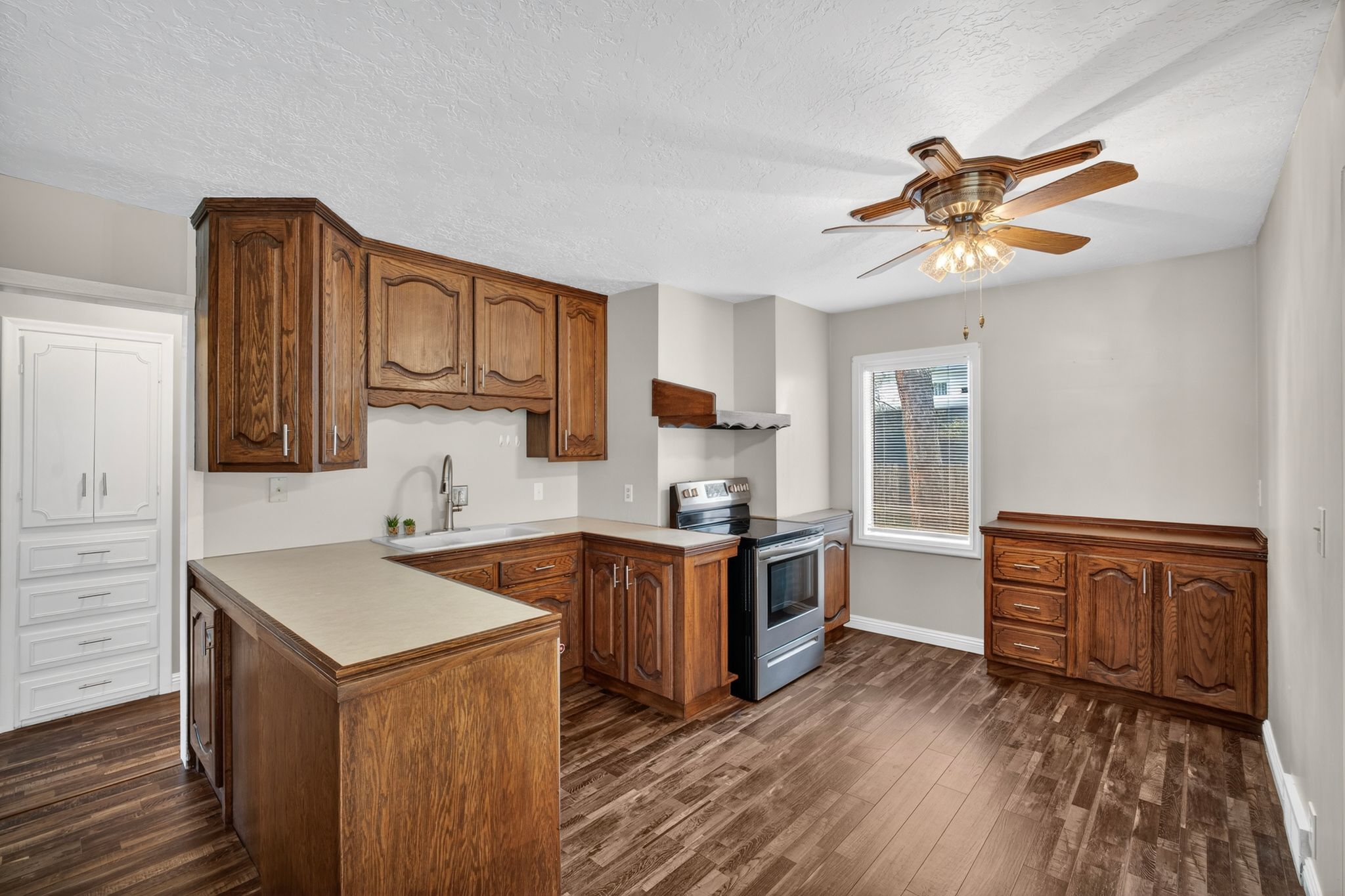 Kitchen featuring wood-finish flooring, wood cabinetry, stainless steel range and range hood, and a built-in white storage cabinet