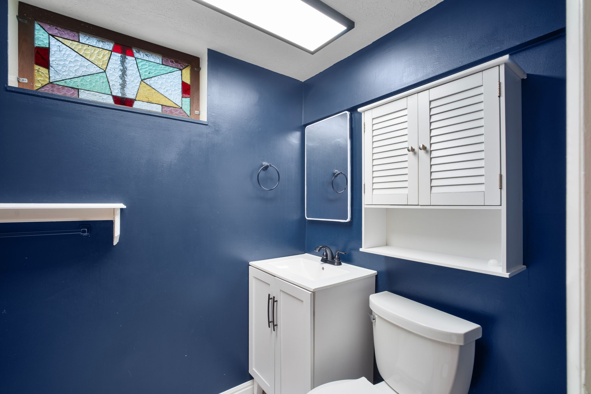 Stained glass window accenting a vanity with a white cabinet, integrated sink, and dark-finish faucet
