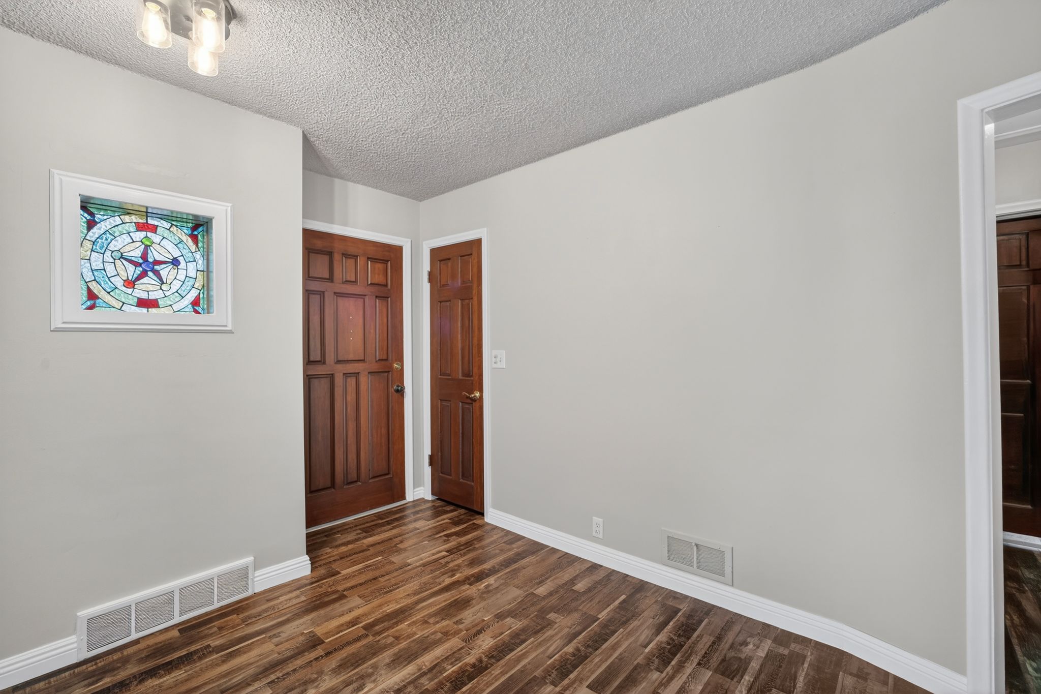 Entryway featuring a decorative stained-glass window, warm wood-finish flooring, paneled interior doors, and crisp white baseboards