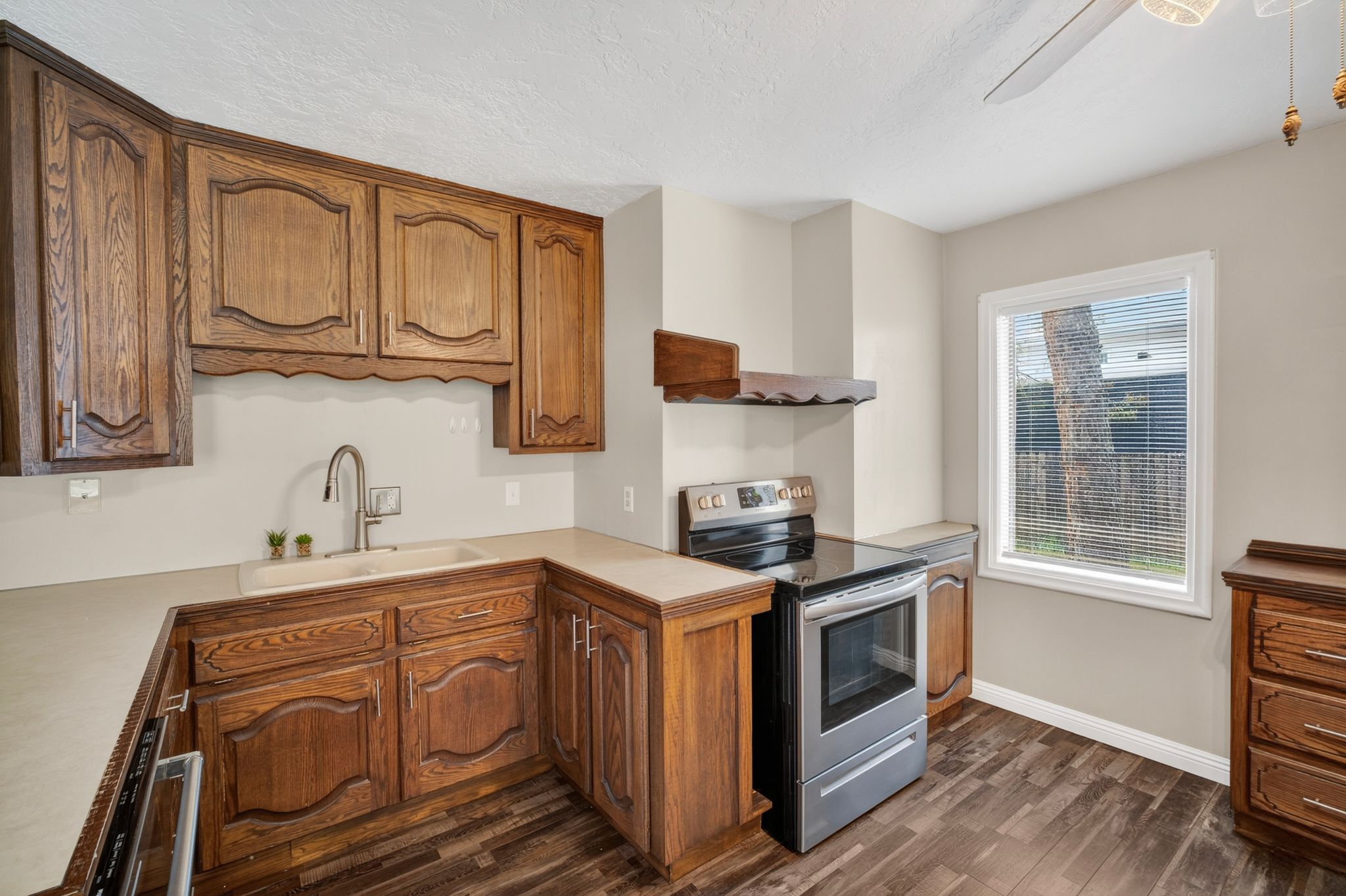 Kitchen featuring wood-finish cabinetry, solid surface countertops, a stainless steel range with ceramic cooktop, and wood-finish flooring
