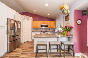 Kitchen featuring wood-finish flooring, stainless steel appliances, upper and lower cabinetry, granite countertops, and a peninsula with seating