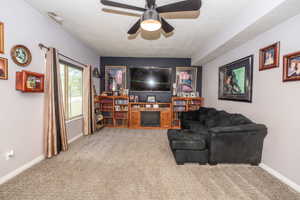 Spacious living area featuring neutral carpet flooring, a dark accent wall, a built-in entertainment center with a fireplace, and a ceiling fan