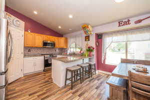 Kitchen featuring wood-finish flooring, a vaulted ceiling, recessed lighting, a stone-finish backsplash, and an island with a stone-finish countertop