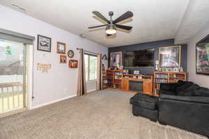 Carpeted living area featuring a ceiling fan with integrated lighting, a sliding glass door providing outdoor access, and a built-in media console with an electric fireplace