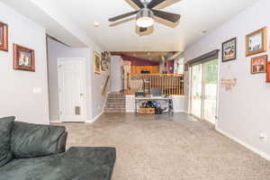Spacious living area featuring light gray walls, a ceiling fan, and carpeted flooring