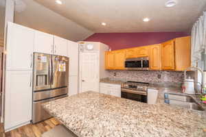 Kitchen featuring a central island with a granite-style countertop, stainless steel appliances, wood-finish flooring, recessed lighting, and a mosaic tile backsplash