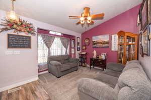 Vaulted ceiling living space featuring a window with transom, wood-finish ceiling fan, and carpet flooring