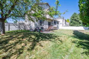 Spacious backyard featuring a large tree providing ample shade, a white privacy fence enclosing the perimeter, a ground-level patio, and exterior vinyl siding