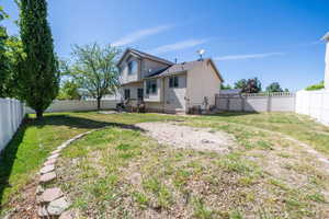 Spacious backyard featuring a two-story residence with beige siding, a partial deck, and a white vinyl fence enclosing the perimeter