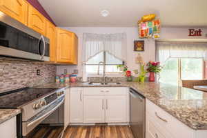 Kitchen featuring stainless steel appliances, wood-finish flooring, white lower cabinetry, natural wood upper cabinetry, and a mosaic tile backsplash