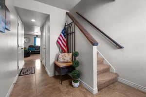 Hallway featuring tile flooring, a carpeted staircase with wood handrails, recessed lighting, and white baseboards