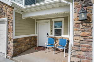 Covered front porch featuring a white entry door, an exterior wall sconce, and a window with horizontal blinds