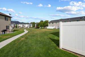 Expansive green space featuring a paved walkway,  white privacy fencing, and mountain backdrop