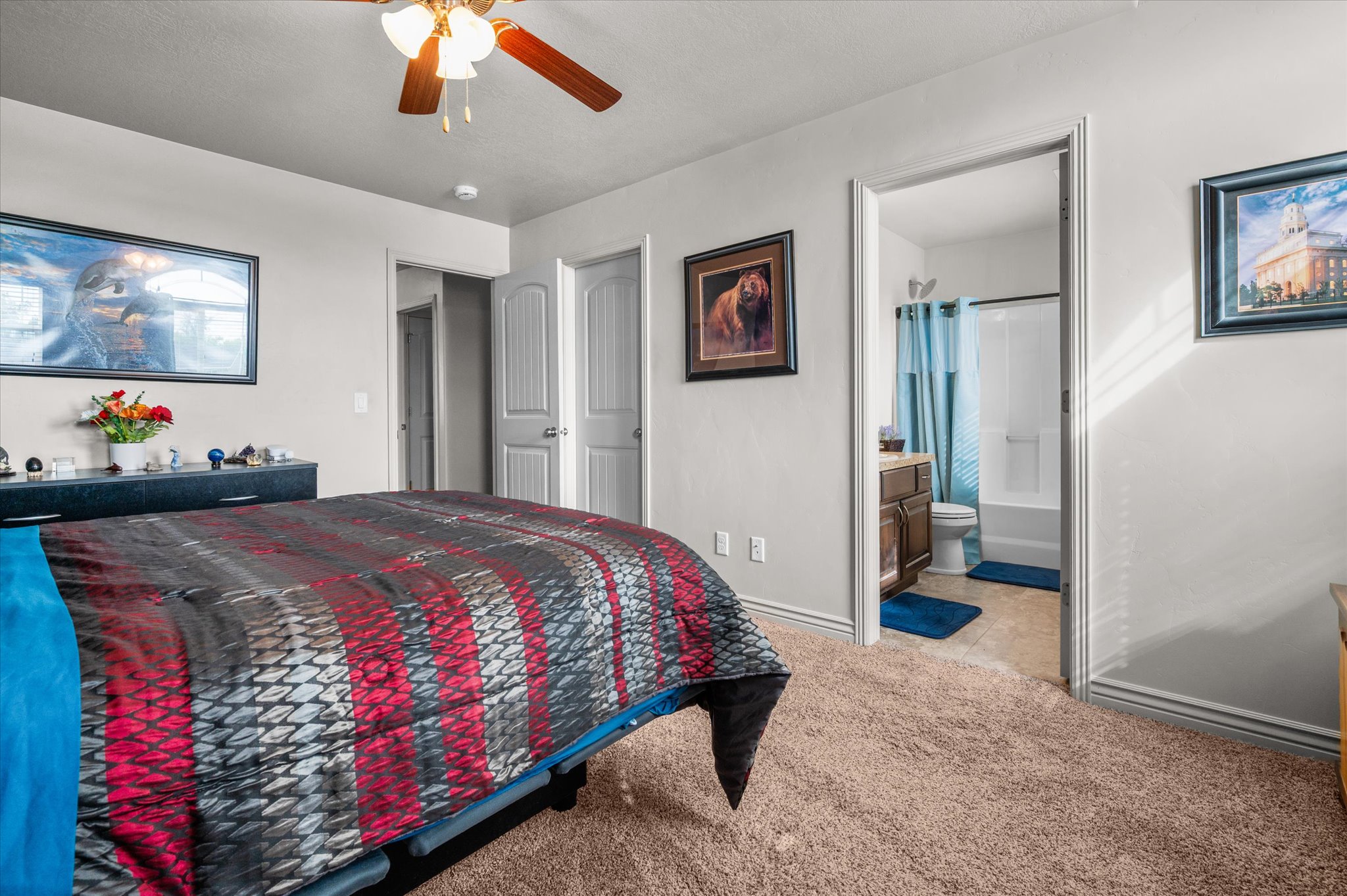 Carpeted bedroom featuring a ceiling fan with light fixture and a framed doorway opening to a full bathroom