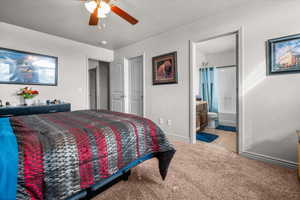 Carpeted bedroom featuring a ceiling fan with light fixture and a framed doorway opening to a full bathroom