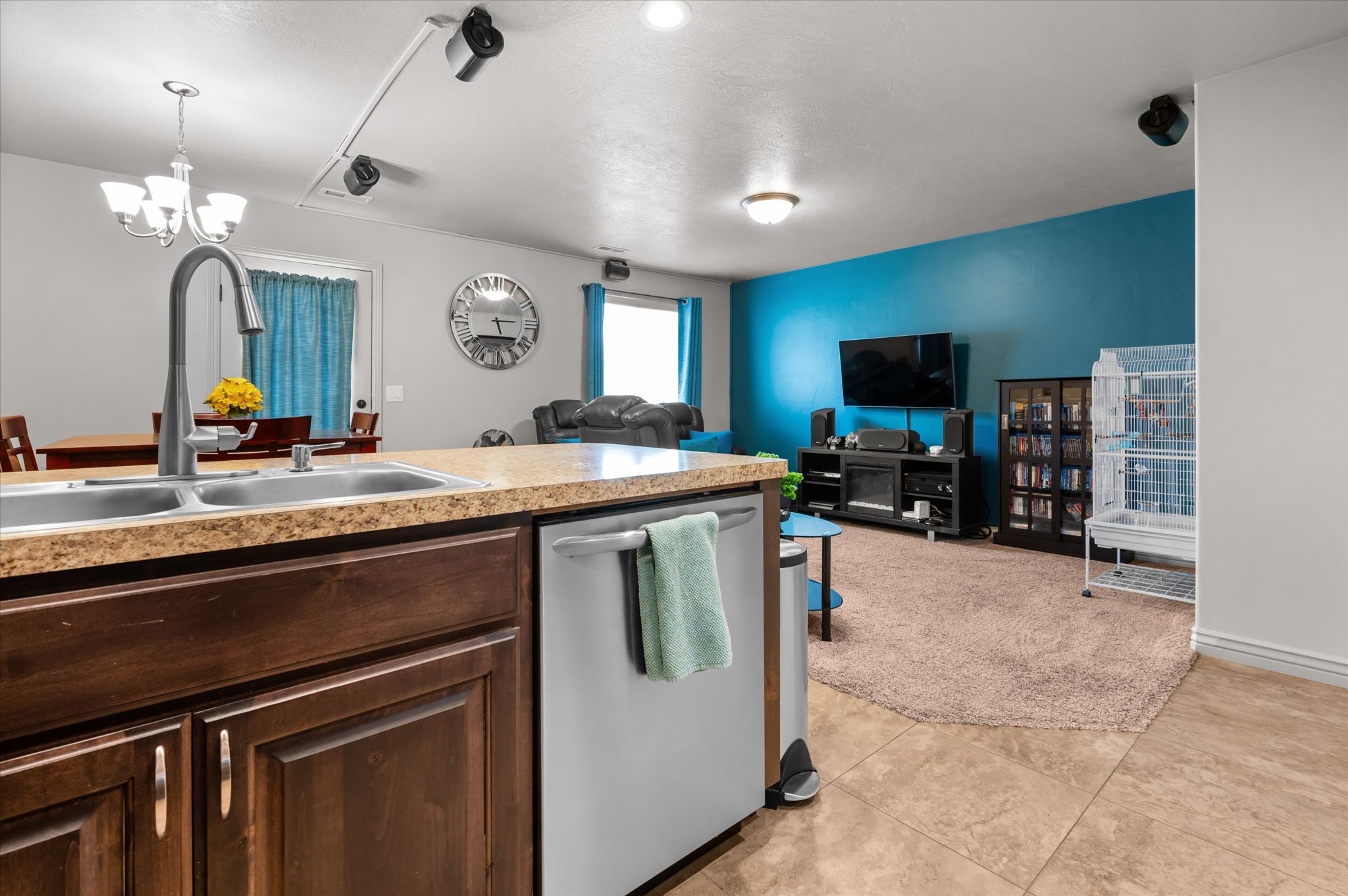 Kitchen island with a double basin sink and a high-arc faucet, rich wood cabinetry, and a built-in dishwasher