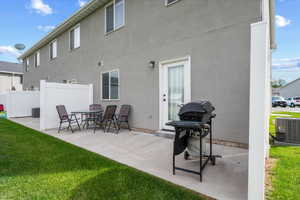 Rear patio with direct access to the interior, featuring a concrete surface, white privacy fencing, and a manicured lawn