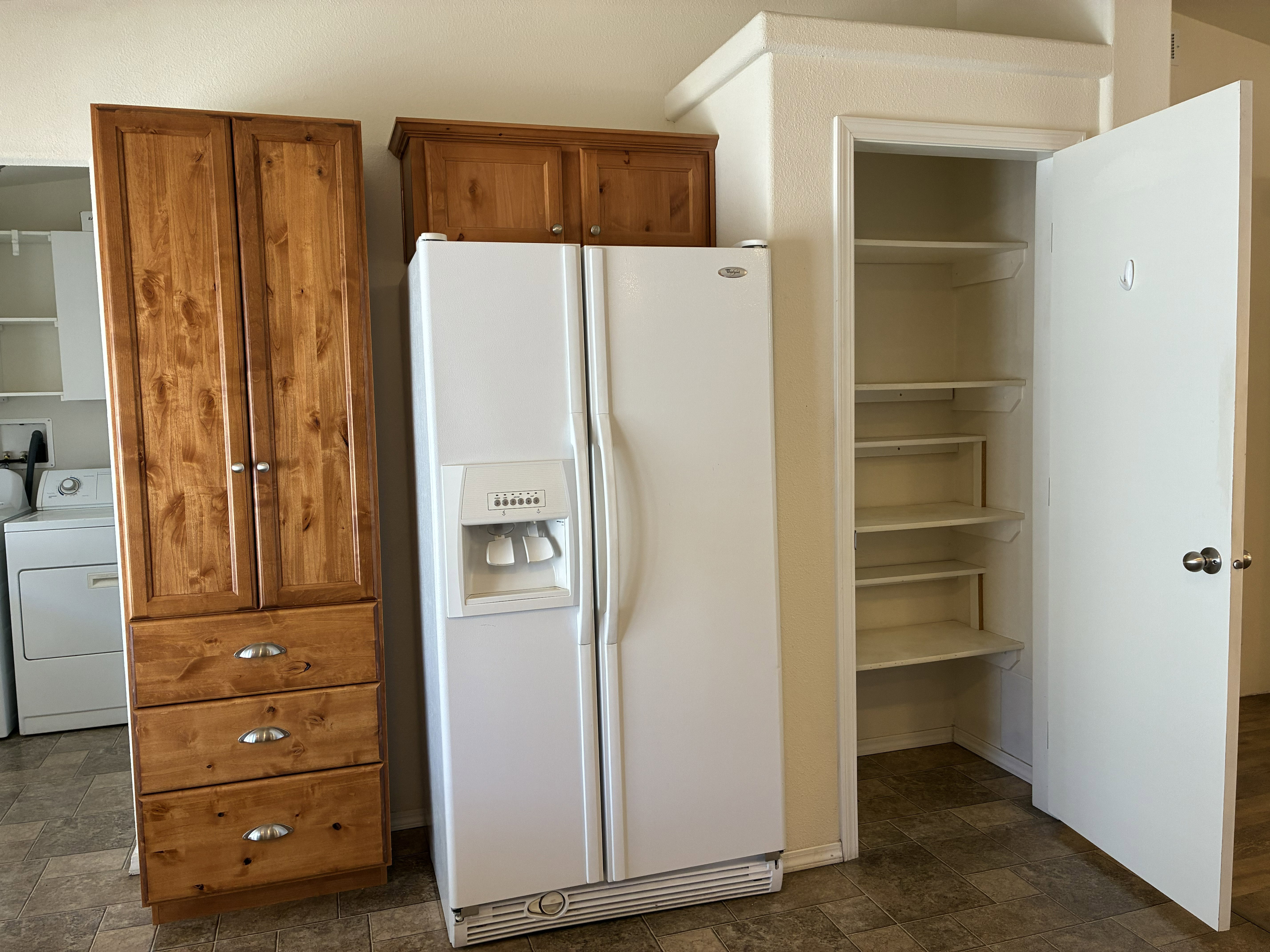 Utility area featuring a side-by-side refrigerator, tall wood-finish cabinetry with drawers, and a pantry with multiple shelves