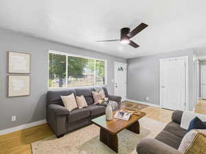 Living area featuring wood-finish flooring, a contemporary ceiling fan with integrated lighting, and a large window with blinds