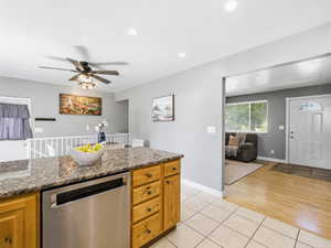 Kitchen island featuring granite-style countertops, light wood cabinetry, and a built-in stainless steel dishwasher