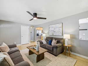 Living area featuring wood-finish flooring, a contemporary ceiling fan, light gray wall tones, and a paneled white door