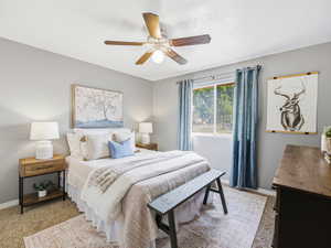 Carpeted bedroom featuring a ceiling fan with light fixture, a window with curtains, and light gray wall paint