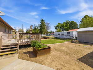 Spacious outdoor area featuring a wood deck, concrete patio, and garden beds