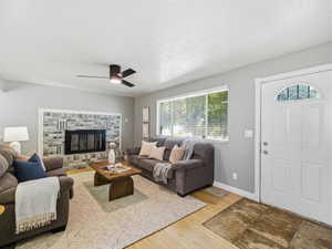 Living area featuring a brick-surround fireplace with a black insert, a ceiling fan, and light wood-finish flooring