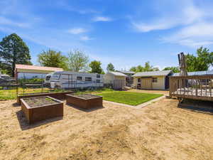 Expansive outdoor space featuring raised planter beds, a manicured lawn area, a wooden deck, and multiple storage sheds