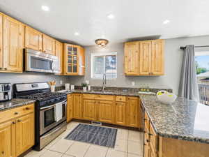 U-shaped kitchen featuring wood cabinetry, stainless steel appliances including a range and microwave, granite countertops, and recessed lighting