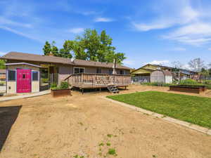 Expansive backyard featuring a wood deck with stairs, a manicured lawn area, two raised garden beds, and a detached storage shed